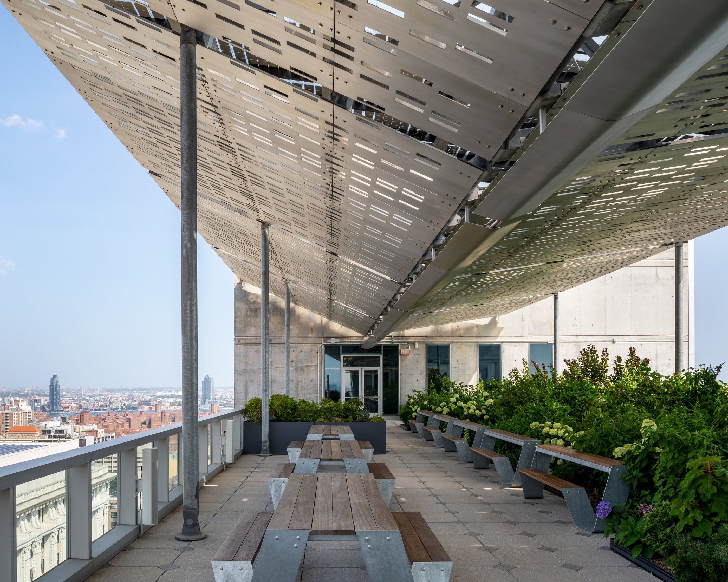 Roof terrace under the perforated canopy, with long tables and planting